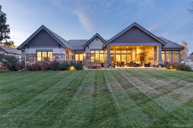 back house at dusk featuring outdoor lounge area, a sunroom, a patio, and a lawn