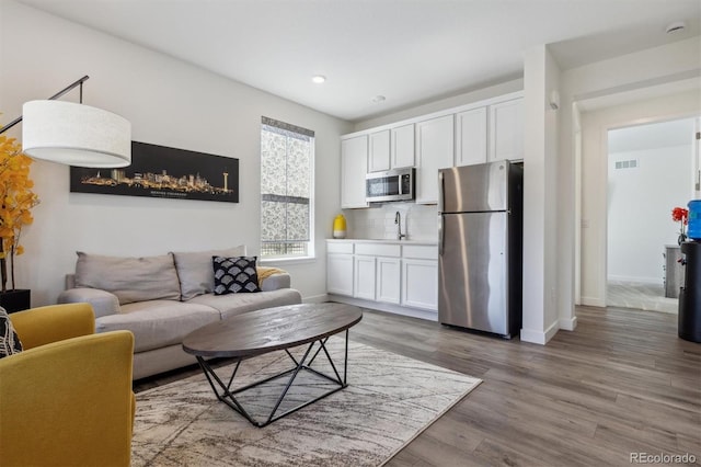 living area with recessed lighting, visible vents, baseboards, and wood finished floors