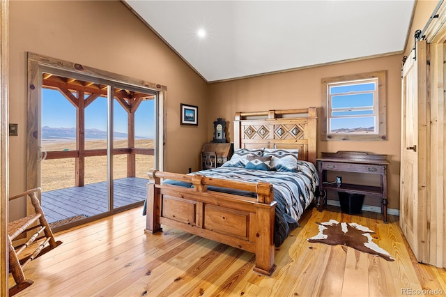 bedroom featuring a barn door, light wood-type flooring, access to exterior, and a mountain view