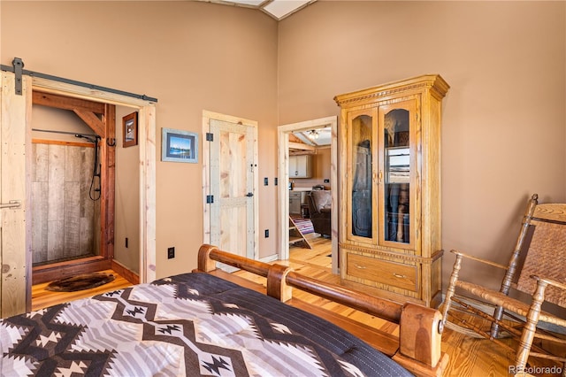 bedroom featuring a towering ceiling, a barn door, and hardwood / wood-style floors