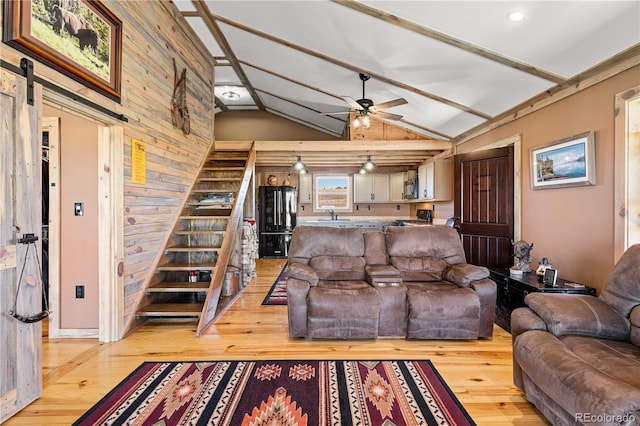 living room with light wood-type flooring, wooden walls, ceiling fan, and vaulted ceiling