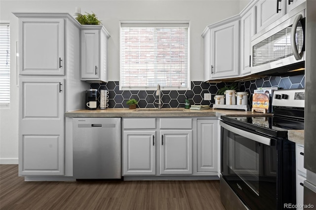 kitchen with appliances with stainless steel finishes, sink, backsplash, white cabinets, and dark hardwood / wood-style flooring