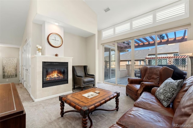 living room with a tile fireplace, light colored carpet, a high ceiling, visible vents, and baseboards