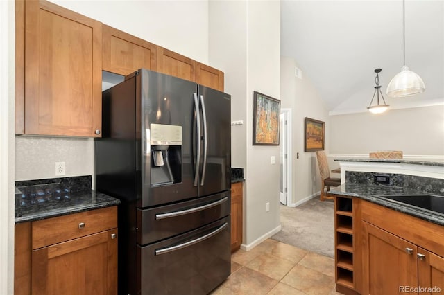 kitchen with brown cabinets, pendant lighting, dark stone countertops, and stainless steel fridge with ice dispenser