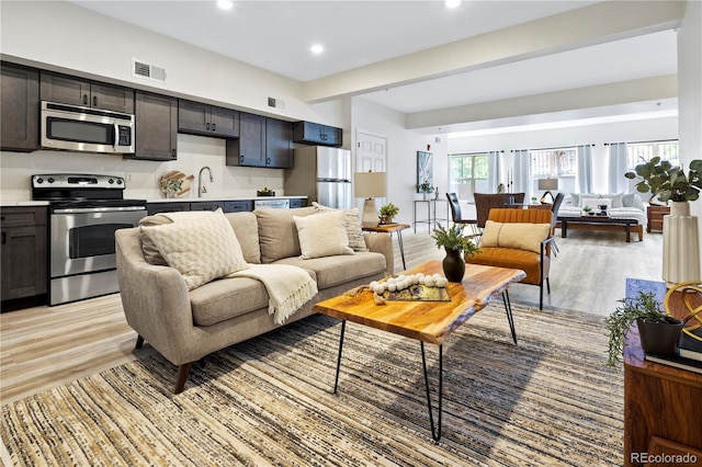 living room with sink, light hardwood / wood-style floors, and beamed ceiling