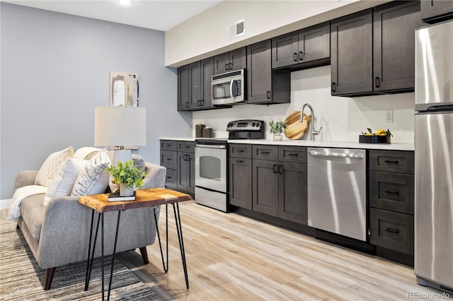 kitchen with dark brown cabinetry, sink, light hardwood / wood-style flooring, and appliances with stainless steel finishes