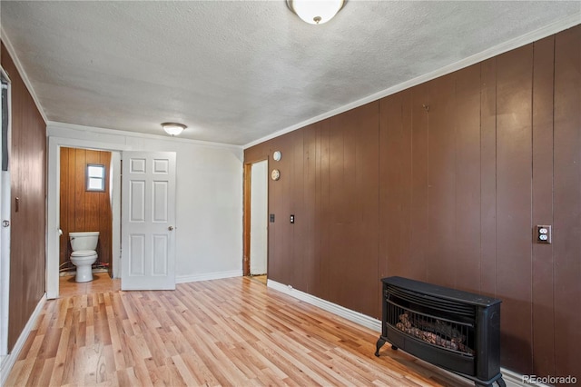 empty room with wooden walls, a wood stove, ornamental molding, heating unit, and light wood-type flooring