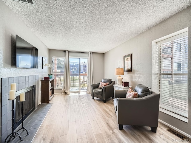 living area featuring a tiled fireplace, visible vents, a textured wall, and wood finished floors