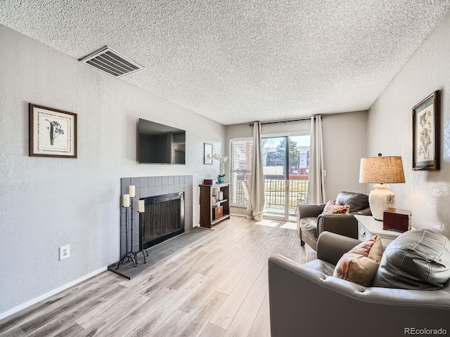 living area featuring visible vents, a tiled fireplace, a textured ceiling, wood finished floors, and a textured wall