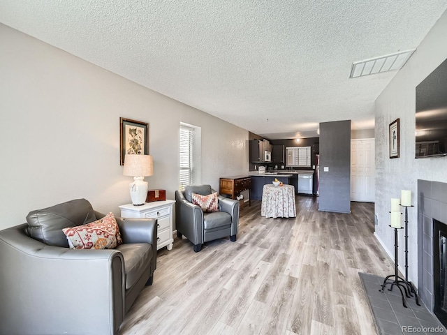 living room with a tiled fireplace, visible vents, a textured ceiling, and light wood-style floors