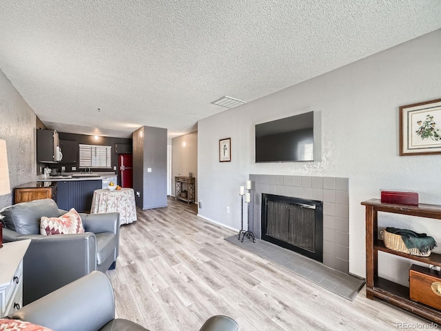 living room with visible vents, a fireplace, a textured ceiling, and light wood-style floors