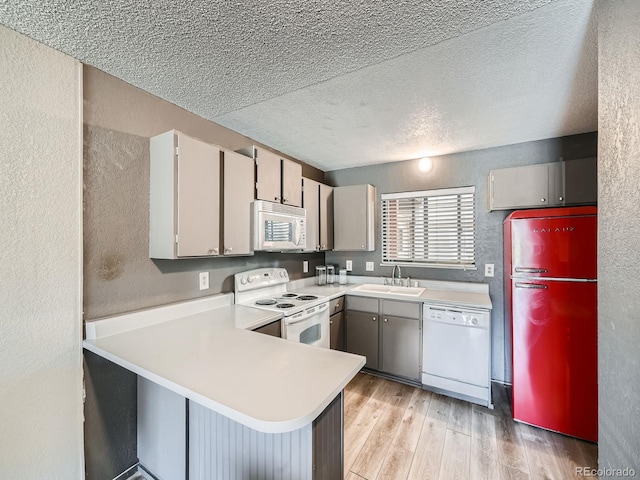 kitchen featuring white appliances, a peninsula, light wood-style flooring, a sink, and light countertops