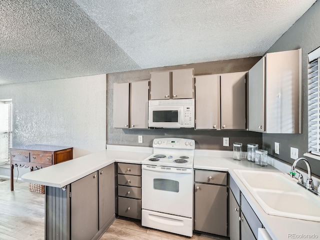 kitchen featuring gray cabinetry, a sink, white appliances, a peninsula, and a textured wall