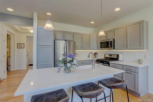 kitchen featuring decorative light fixtures, a center island with sink, a kitchen bar, gray cabinets, and appliances with stainless steel finishes