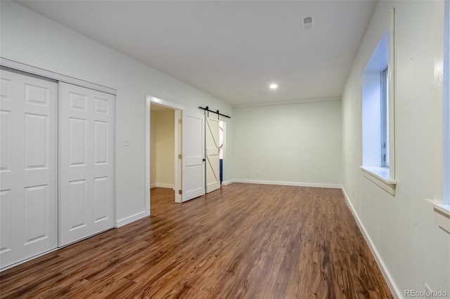 unfurnished bedroom with a closet, a barn door, and wood-type flooring