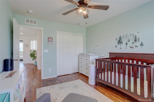 bedroom featuring a crib, a closet, ceiling fan, and light wood-type flooring