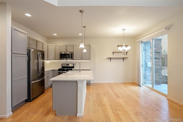 kitchen with a kitchen island with sink, appliances with stainless steel finishes, hanging light fixtures, light hardwood / wood-style floors, and gray cabinetry