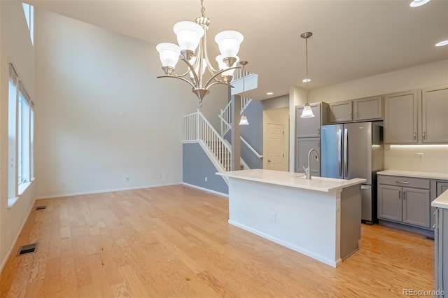 kitchen featuring gray cabinetry, a chandelier, decorative light fixtures, and a center island with sink