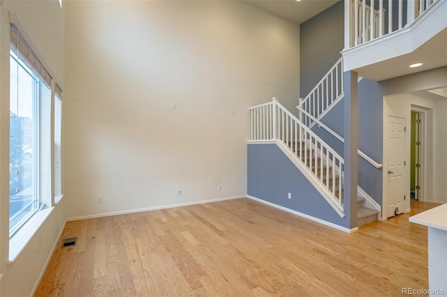 unfurnished living room featuring a towering ceiling and light hardwood / wood-style floors