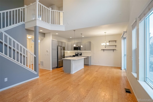 kitchen with gray cabinetry, stainless steel appliances, light wood-type flooring, pendant lighting, and a kitchen island