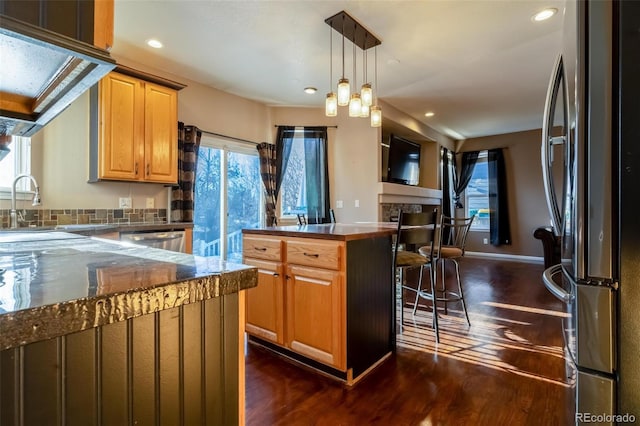 kitchen featuring stainless steel appliances, pendant lighting, dark hardwood / wood-style floors, a kitchen island, and a breakfast bar area