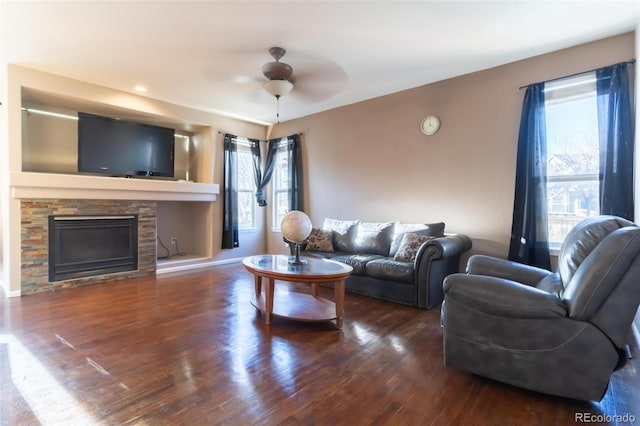 living room featuring dark hardwood / wood-style floors, ceiling fan, and a stone fireplace