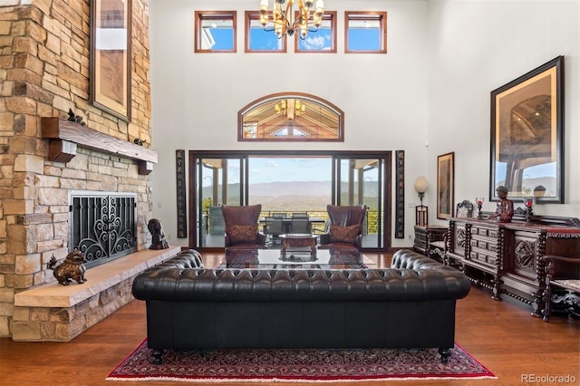 living room featuring a high ceiling, wood-type flooring, a stone fireplace, and an inviting chandelier