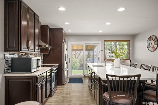 kitchen featuring appliances with stainless steel finishes, a kitchen bar, a sink, light countertops, and recessed lighting