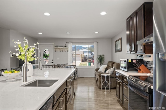 kitchen featuring appliances with stainless steel finishes, a sink, wall chimney range hood, light wood-type flooring, and recessed lighting
