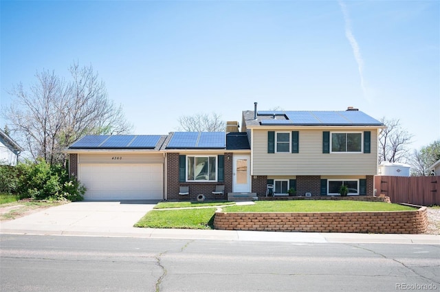 split level home with an attached garage, brick siding, concrete driveway, and roof mounted solar panels