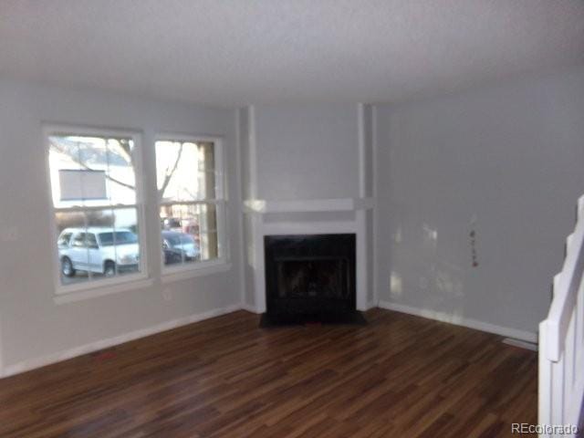 unfurnished living room featuring a fireplace with flush hearth, baseboards, and dark wood-style floors