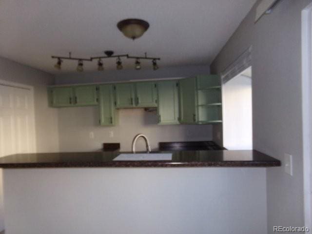 kitchen with green cabinets, a peninsula, dark countertops, and a sink