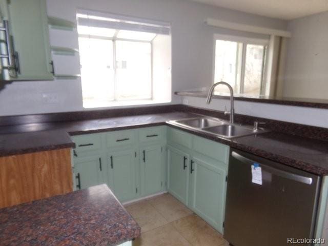 kitchen with light tile patterned floors, dark countertops, stainless steel dishwasher, open shelves, and a sink