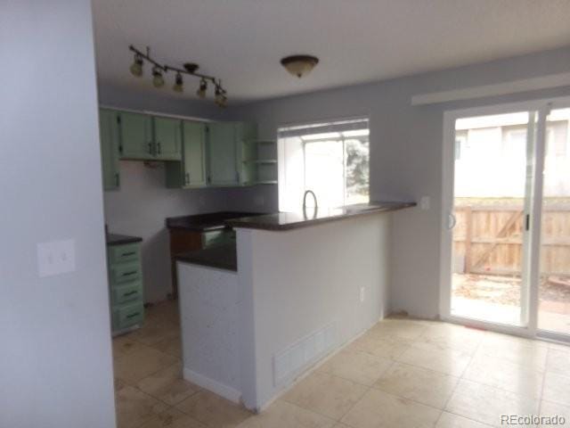 kitchen with a peninsula, visible vents, green cabinets, dark countertops, and rail lighting