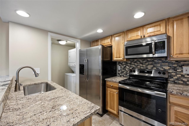 kitchen featuring stacked washer and dryer, stainless steel appliances, tasteful backsplash, light stone countertops, and sink