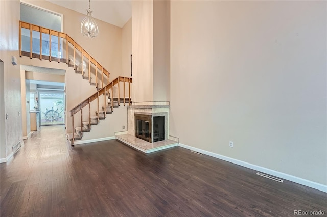 unfurnished living room featuring a high ceiling, a notable chandelier, a healthy amount of sunlight, and dark hardwood / wood-style flooring