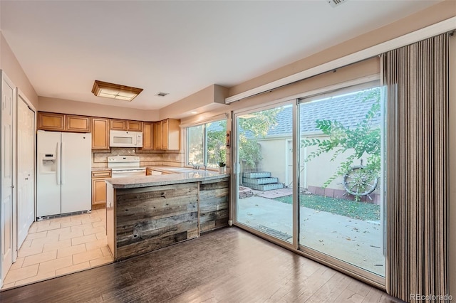 kitchen featuring kitchen peninsula, backsplash, light hardwood / wood-style floors, light stone counters, and white appliances