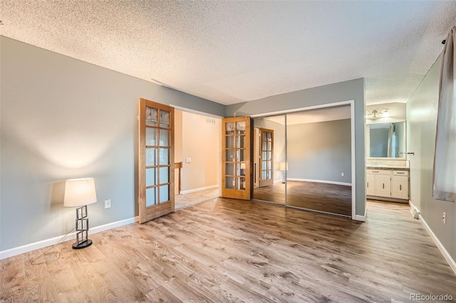 spare room with light hardwood / wood-style floors, french doors, and a textured ceiling