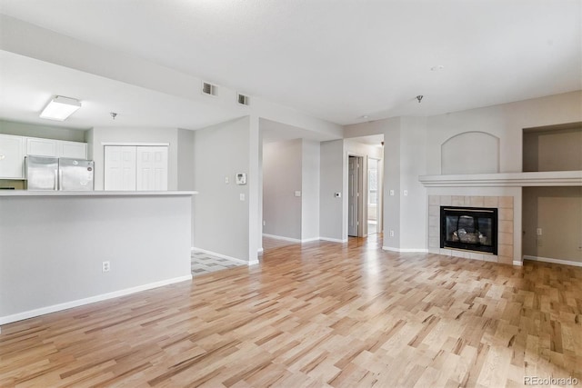 unfurnished living room with a tiled fireplace, baseboards, light wood-style flooring, and visible vents