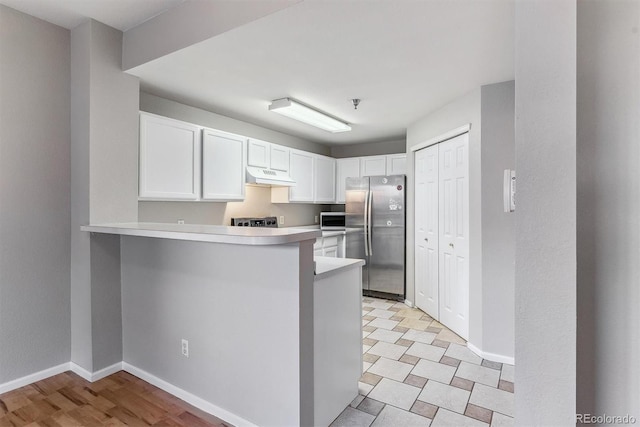 kitchen with freestanding refrigerator, baseboards, light countertops, under cabinet range hood, and white cabinets