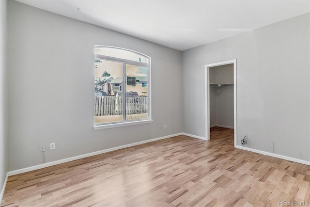 unfurnished bedroom with baseboards, a closet, wood finished floors, and a spacious closet