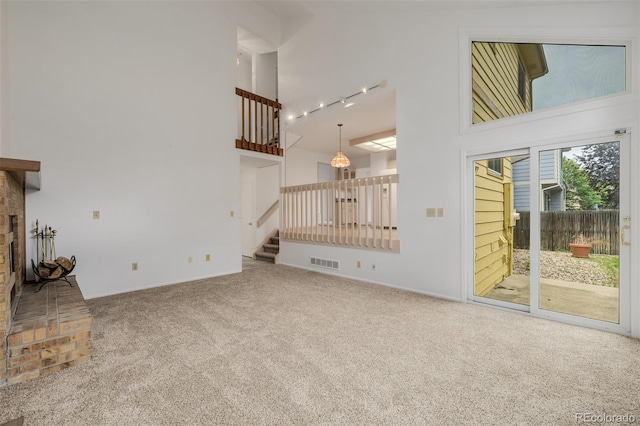 12319 W Burgundy Ave, Littleton, CO 80127 - unfurnished living room with carpet flooring, stairs, a high ceiling, a fireplace with raised hearth, and rail lighting