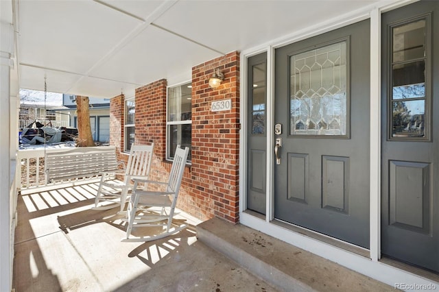 property entrance with a porch and brick siding