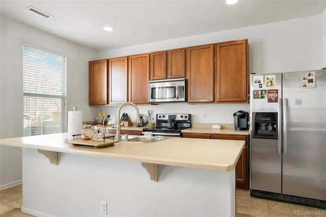 kitchen with light tile patterned floors, a breakfast bar, an island with sink, and appliances with stainless steel finishes