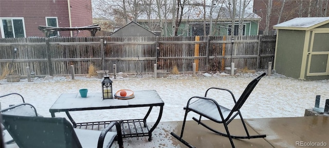 snow covered patio featuring a shed, an outdoor structure, and a fenced backyard