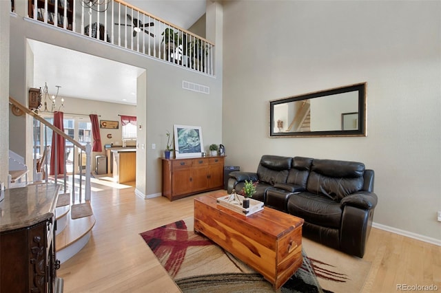 living room with a chandelier, light hardwood / wood-style flooring, and a towering ceiling