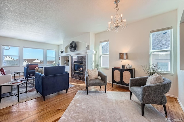 living room with a chandelier, a textured ceiling, a fireplace, and light hardwood / wood-style floors