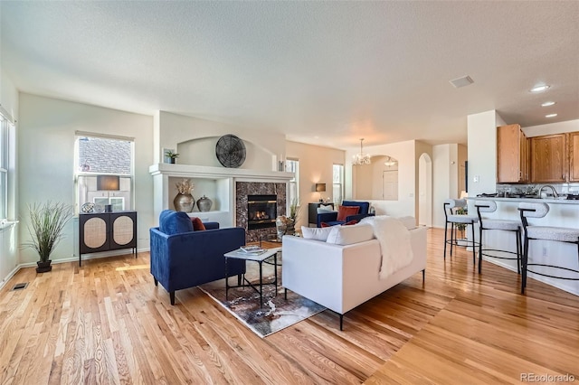 living room featuring an inviting chandelier, a high end fireplace, a textured ceiling, and light wood-type flooring