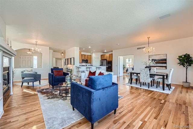 living room featuring light wood-type flooring, a textured ceiling, and a chandelier