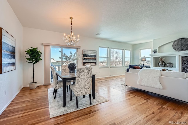 dining space with a textured ceiling, a notable chandelier, and light hardwood / wood-style floors